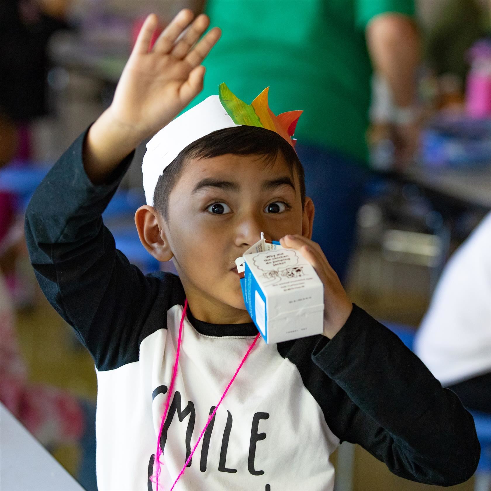  Elementary student waving while drinking a carton of milk